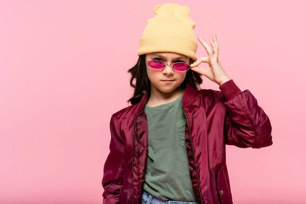 Niña preadolescente en traje de moda ajustando gafas de sol aisladas en rosa - foto de stock