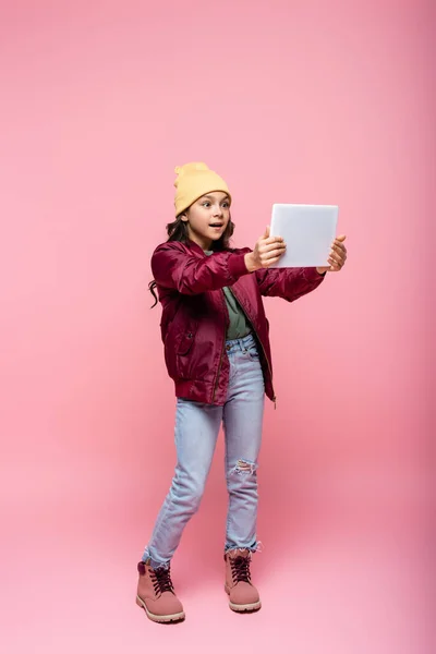 Longitud completa de la chica preadolescente con estilo en traje de moda utilizando tableta digital en rosa - foto de stock