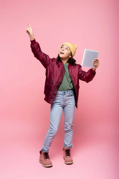 Full length of stylish preteen girl holding digital tablet and pointing with finger on pink — Stock Photo