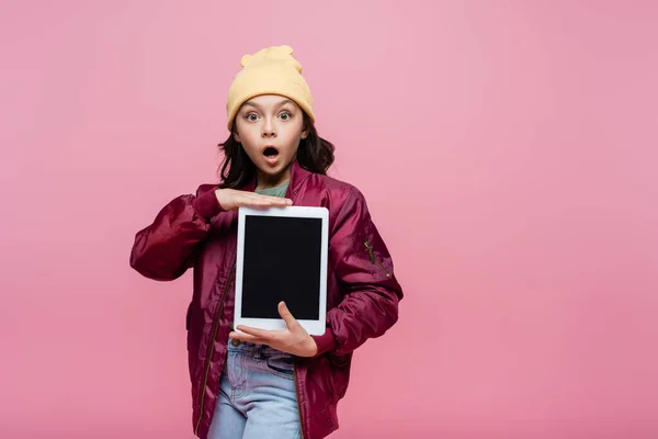 Schockiertes Mädchen im trendigen Outfit hält digitales Tablet mit leerem Bildschirm isoliert auf rosa — Stockfoto