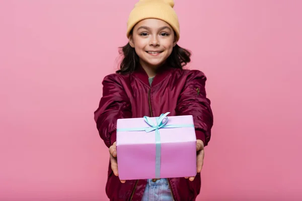 Happy preteen girl in trendy outfit holding wrapped present isolated on pink — Stock Photo