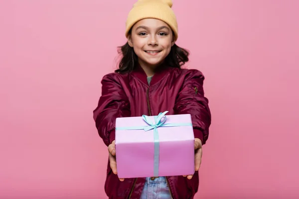 Menina pré-adolescente feliz na roupa da moda segurando presente envolto isolado em rosa — Fotografia de Stock