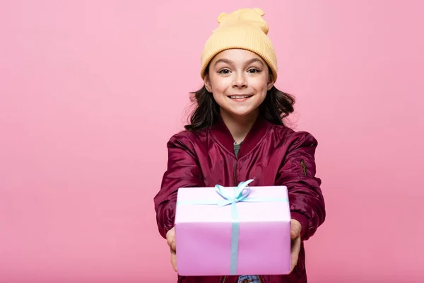 Joyful preteen girl in trendy outfit holding wrapped present isolated on pink — Stock Photo