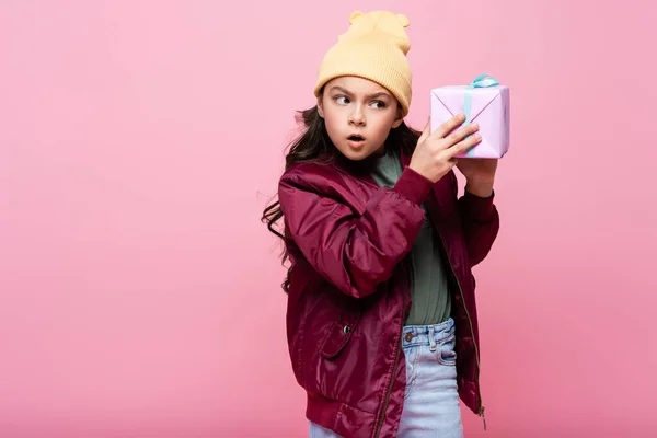 Neugierige Frühchen im trendigen Outfit schütteln Geschenk isoliert auf rosa — Stockfoto