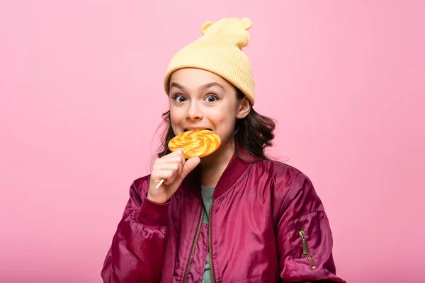 Trendy preteen girl im Winter-Outfit beißt Lutscher isoliert auf rosa — Stockfoto