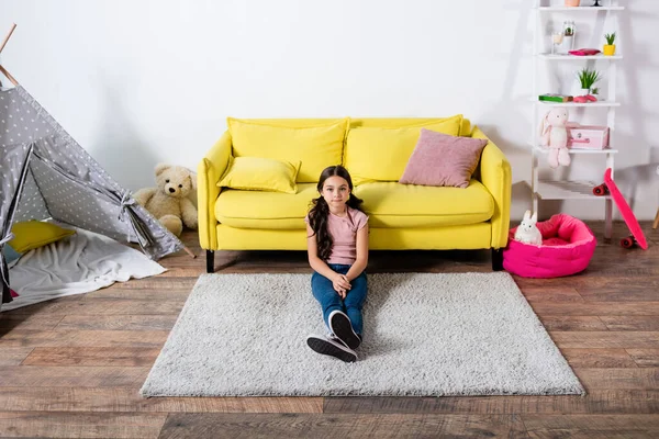 Blick von oben auf ein Frühchen, das auf einem Teppich im modernen Wohnzimmer sitzt — Stockfoto