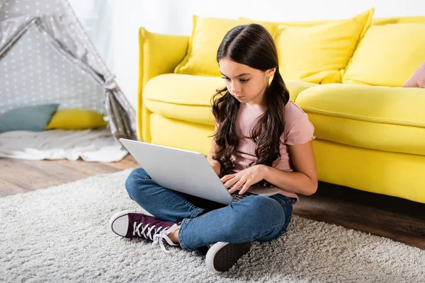 Frühchen-Mädchen sitzt auf Teppich und benutzt Laptop im modernen Wohnzimmer — Stockfoto