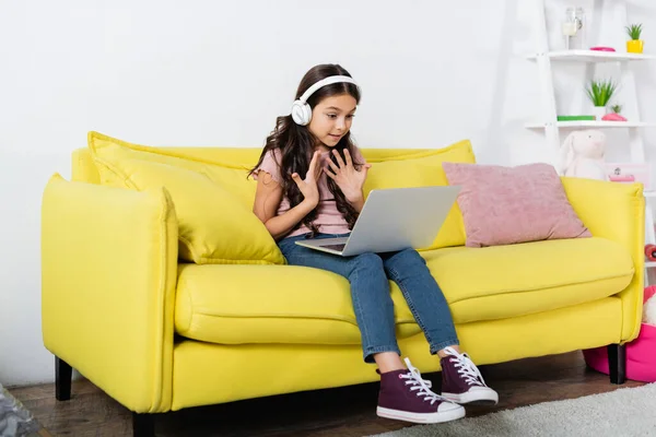 Menina pré-adolescente em fones de ouvido sem fio falando durante a chamada de vídeo enquanto estuda on-line em casa — Fotografia de Stock