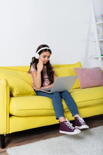 Frühchen-Mädchen in drahtlosen Kopfhörern hebt die Hand, während sie zu Hause online lernt — Stockfoto
