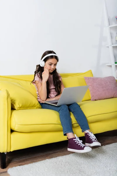 Preteen fille dans sans fil casque levant la main tout en étudiant en ligne à la maison — Photo de stock