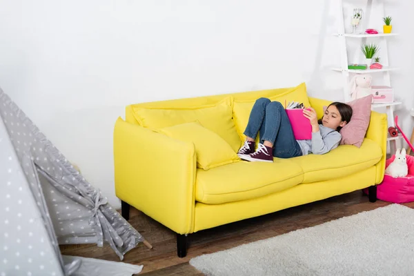 Preteen child reading book while lying on couch at home — Stock Photo