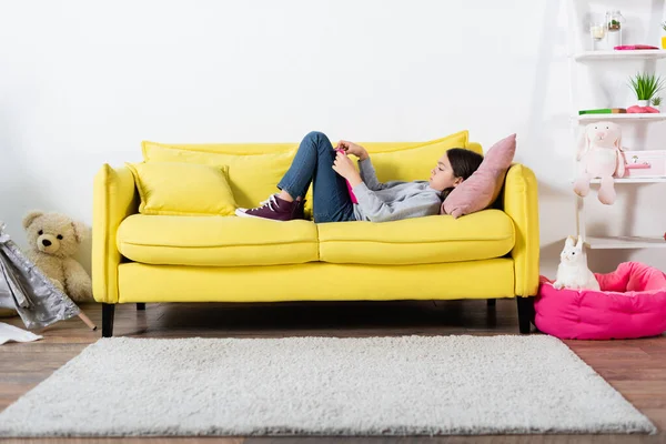 Seitenansicht eines frühgeborenen Mädchens, das Buch liest, während es zu Hause auf der Couch liegt — Stockfoto