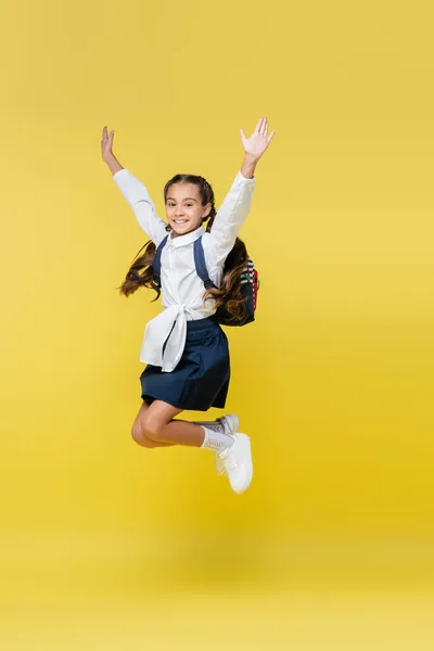 Cheerful schoolgirl with backpack jumping on yellow — Stock Photo
