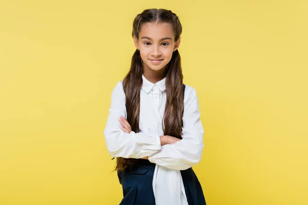 Smiling schoolgirl with crossed arms looking at camera isolated on yellow — Stock Photo