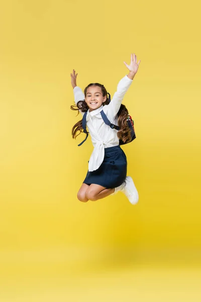 Positive schoolkid jumping and looking at camera on yellow — Stock Photo