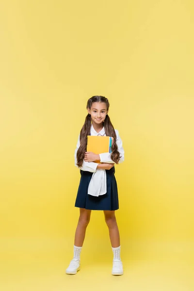 Full length of smiling schoolgirl holding notebooks on yellow background — Stock Photo