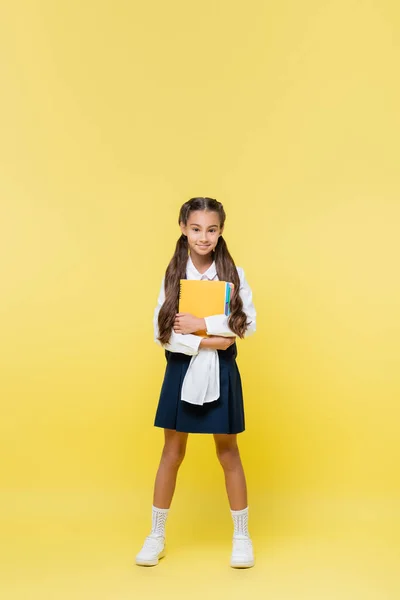 Volle Länge des lächelnden Schulmädchens mit Notizbüchern auf gelbem Hintergrund — Stockfoto