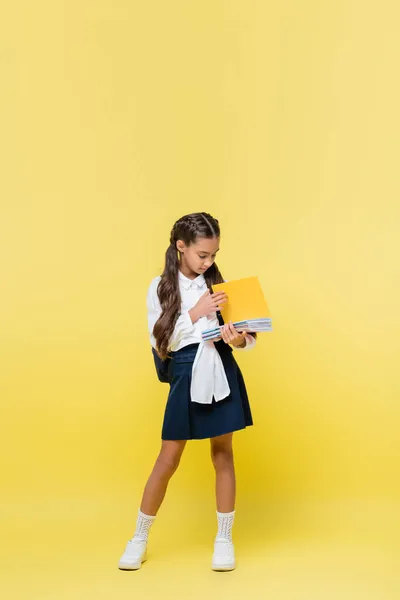 Schoolgirl holding notebooks while standing on yellow background — Stock Photo