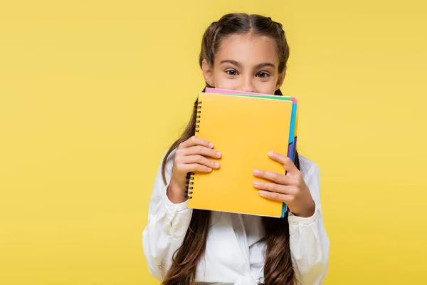 Schoolgirl covering face with notebooks isolated on yellow — Stock Photo