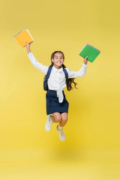 Happy schoolkid with backpack and notebooks jumping on yellow — Stock Photo