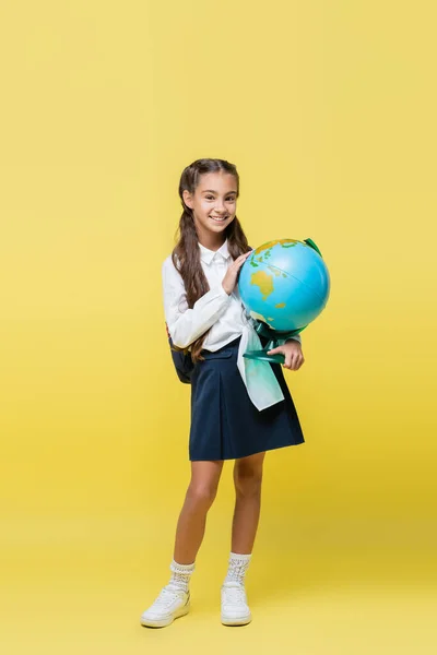Smiling schoolgirl holding globe on yellow background — Stock Photo