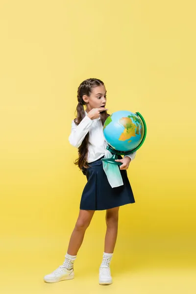 Full length of schoolgirl pointing at globe on yellow background — Stock Photo