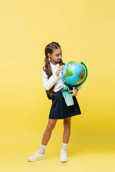 Escolar com mochila segurando globo no fundo amarelo — Fotografia de Stock