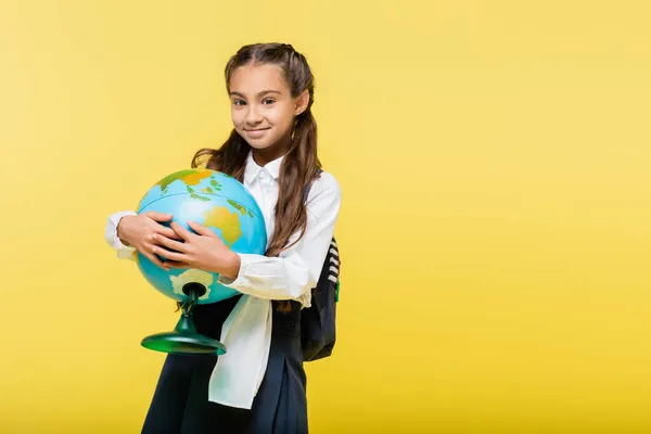 Школярка тримає глобус і посміхається на камеру ізольовано на жовтому — стокове фото