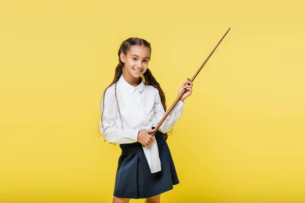 Positive schoolgirl with pointer looking at camera isolated on yellow — Stock Photo