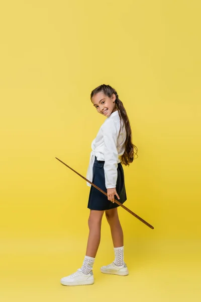 Escolar sonriente sosteniendo el puntero y mirando a la cámara sobre fondo amarillo - foto de stock