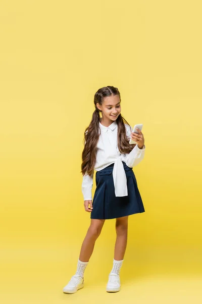 Écolier souriant utilisant un smartphone sur fond jaune — Photo de stock