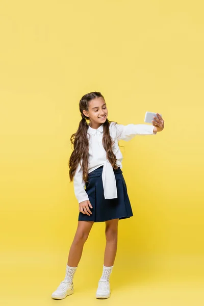 Школьник в полный рост делает селфи на смартфоне на желтом фоне — стоковое фото