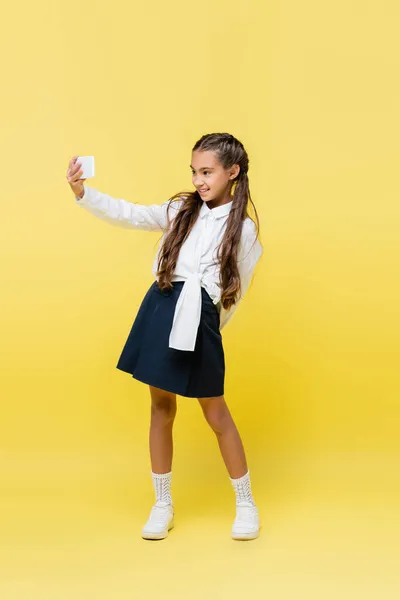 Escolar sonriente tomando selfie en el teléfono celular sobre fondo amarillo - foto de stock