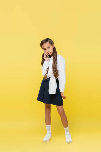 Full length of schoolgirl talking on smartphone on yellow background — Stock Photo