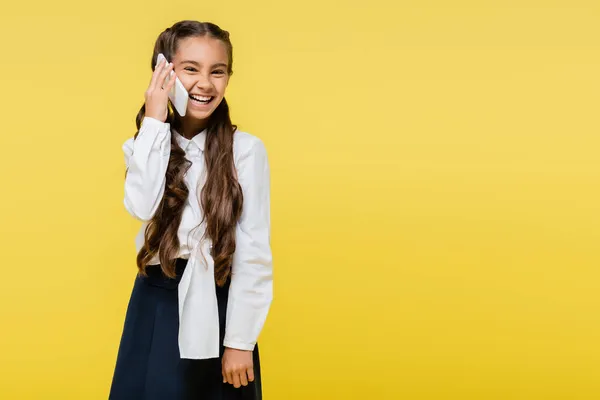Весела школярка розмовляє на мобільному телефоні ізольовано на жовтому — стокове фото