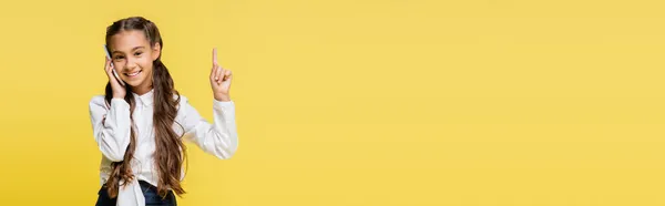 Lächelndes Schulkind im Hemd, das mit dem Smartphone spricht und mit dem Finger auf gelbes Banner zeigt — Stockfoto