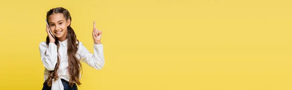 Estudante sorrindo na camisa falando no smartphone e apontando com o dedo isolado no amarelo, banner — Fotografia de Stock