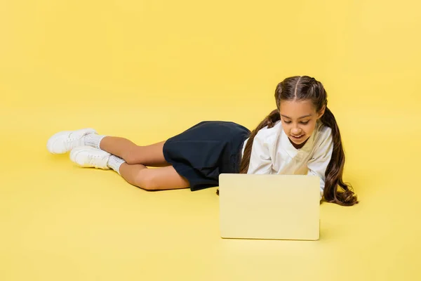 Estudante em camisa usando laptop enquanto deitado no fundo amarelo — Fotografia de Stock
