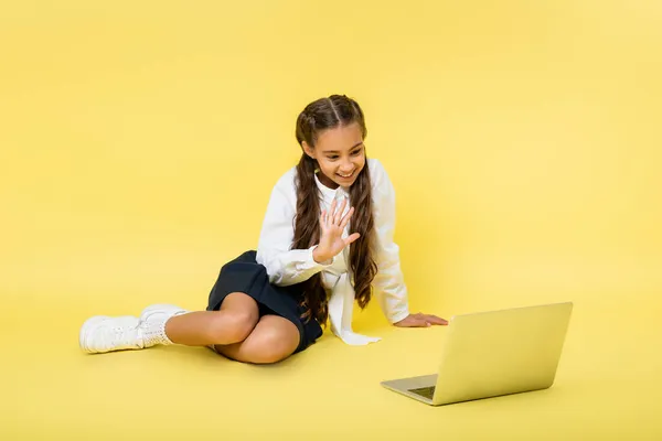 Estudante sorrindo ter chamada de vídeo no laptop no fundo amarelo — Fotografia de Stock