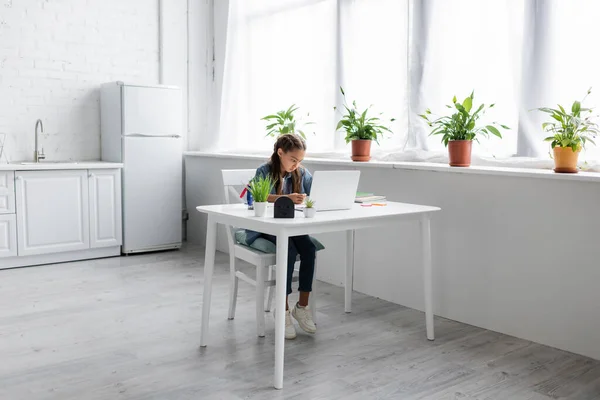 Preteen girl using laptop near notebooks in kitchen — Stock Photo