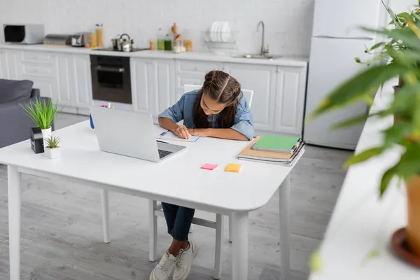 Bambino preadolescente che fa i compiti vicino a copiare libri e laptop in cucina a casa — Foto stock