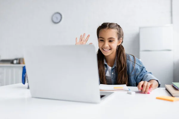 Smiling schoolgirl having video call on blurred laptop in kitchen — Stock Photo