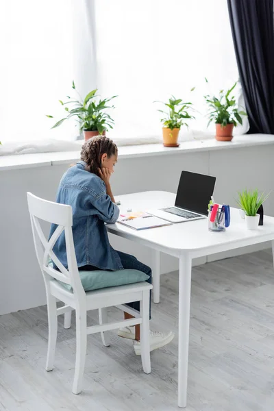 Estudante fazendo lição de casa perto do laptop com tela em branco e notebook em casa — Fotografia de Stock