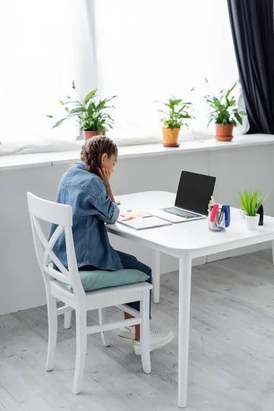 Colegiala haciendo tarea cerca de la computadora portátil con pantalla en blanco y portátil en casa - foto de stock