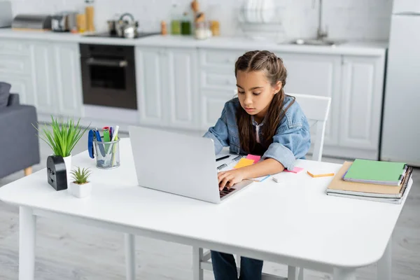 Bambino preadolescente che utilizza il computer portatile durante l'educazione online vicino a copiare libri e piante a casa — Foto stock