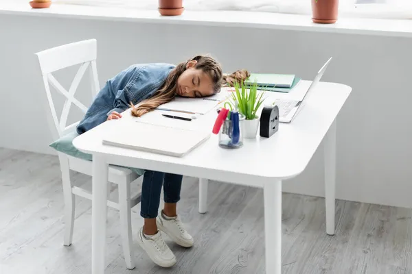 Preteen girl sleeping near stationery and laptop on table at home — Stock Photo