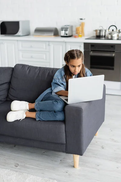 Preteen kid using laptop while sitting on couch at home — Stockfoto