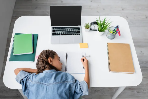 Top view of kid sleeping near copy books and laptop with blank screen on table — Stock Photo