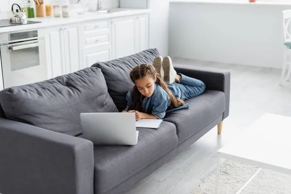 Niño mirando portátil cerca de la computadora portátil durante la educación en línea en el hogar - foto de stock
