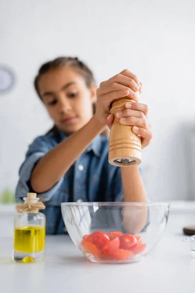Розмита дитина приправляє вишневі помідори в мисці біля оливкової олії на кухні — стокове фото